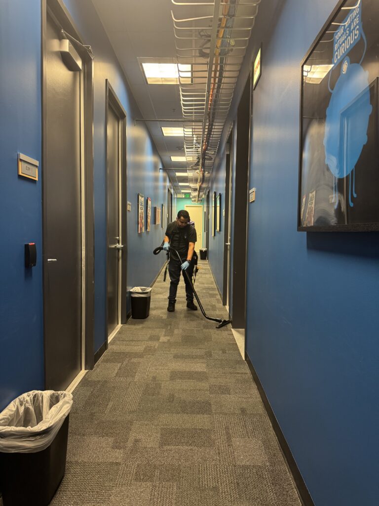 Person cleaning the hallway with a vacuum cleaner, wearing gloves and a backpack.
