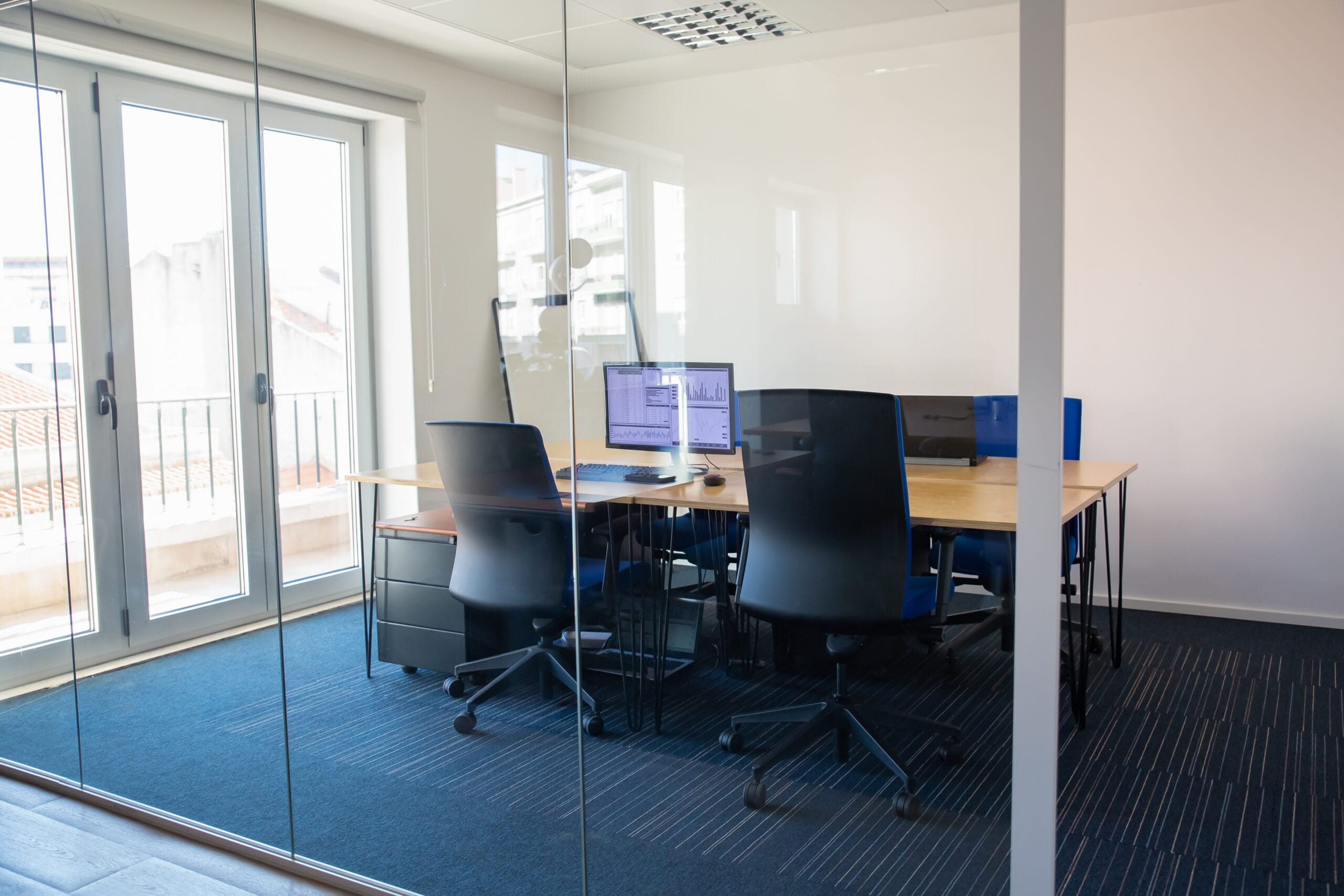 Empty office conference room with two monitors, black chairs, and a glass wall.