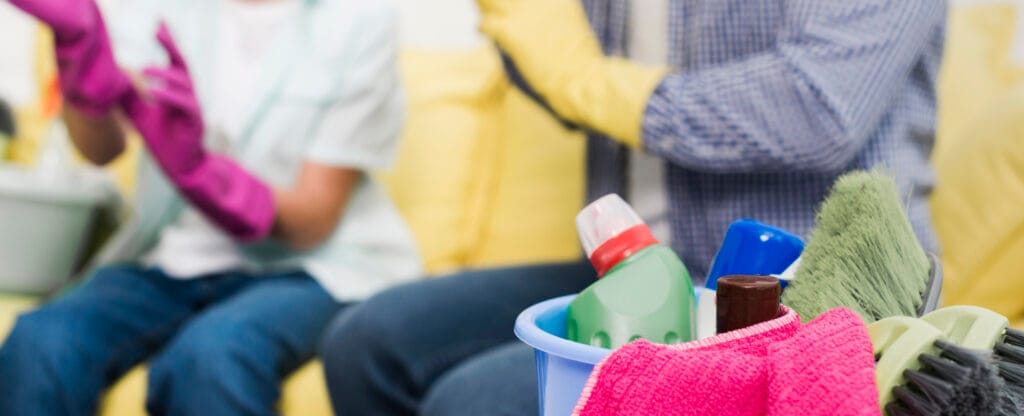 People wearing gloves sitting with cleaning supplies in a bucket.