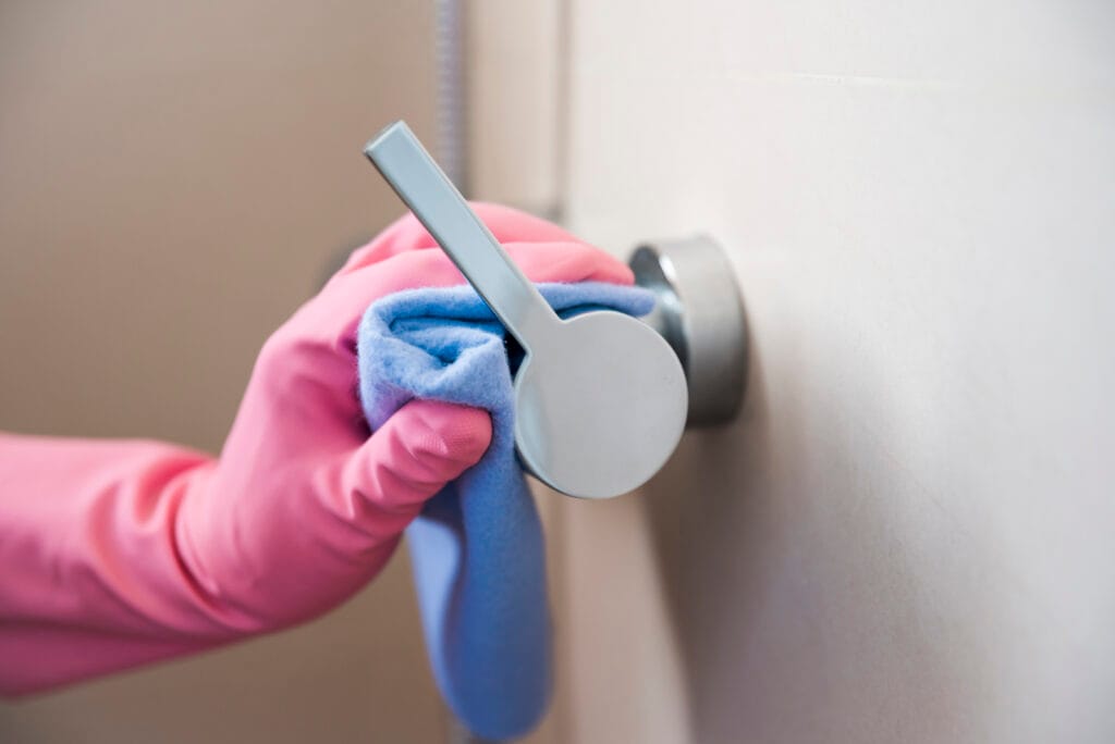 Hand wearing a pink glove cleaning a door handle with a blue cloth.