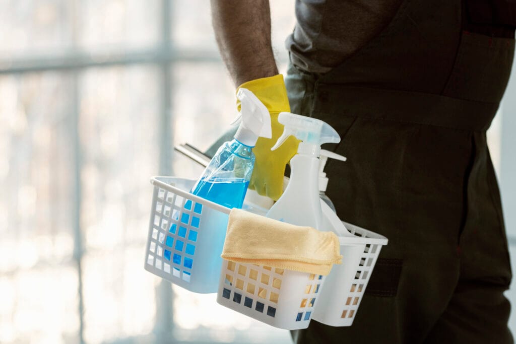 Person holding a cleaning caddy with spray bottles, cloth, and cleaning supplies.
