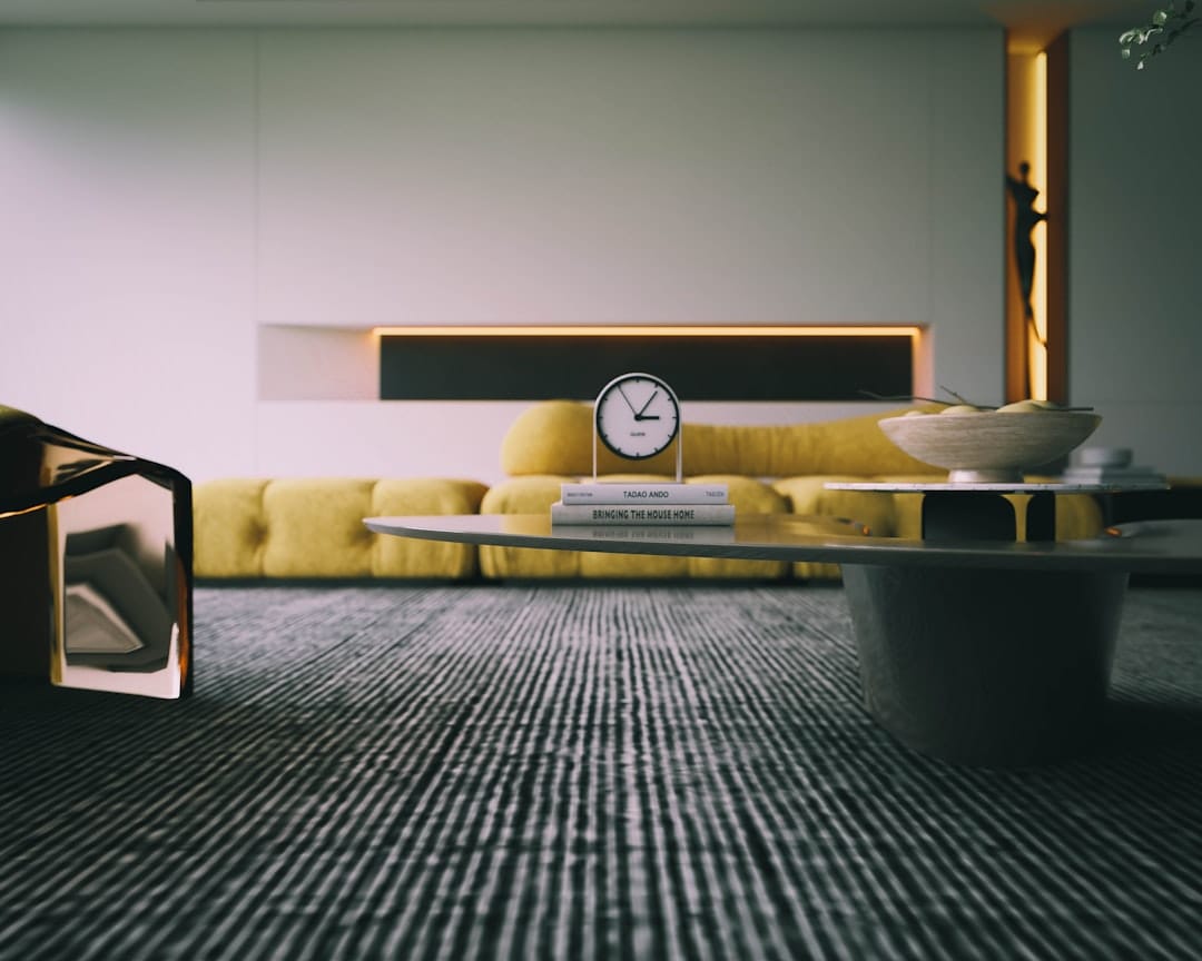 A modern living room with a yellow sofa, a low coffee table, and a wall clock on top of books.