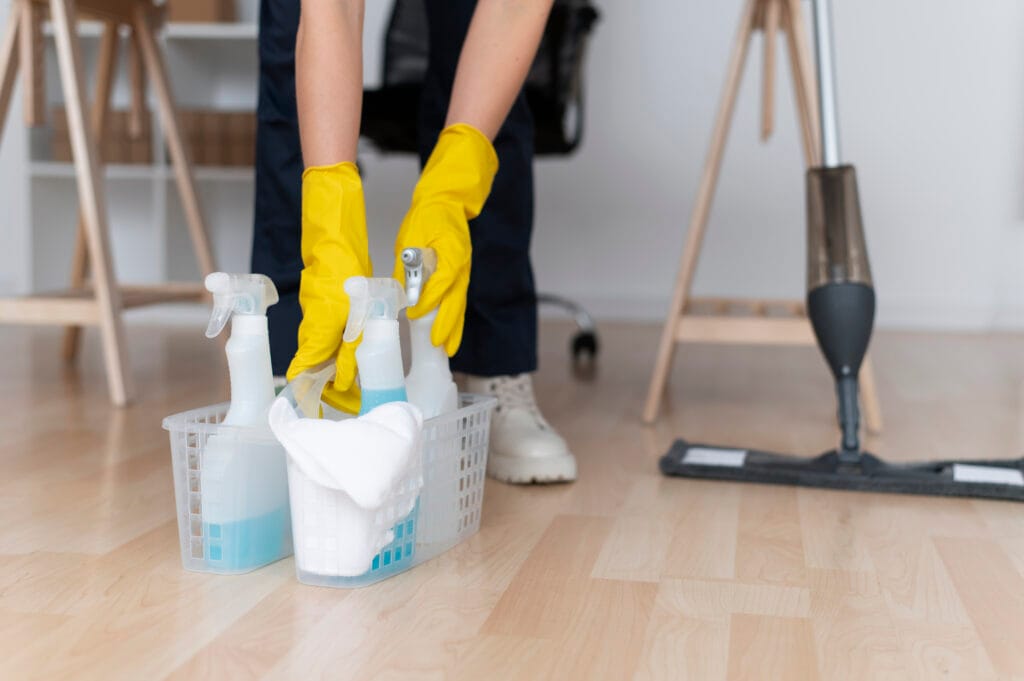 Person wearing yellow gloves cleaning spray bottles on a wooden floor.