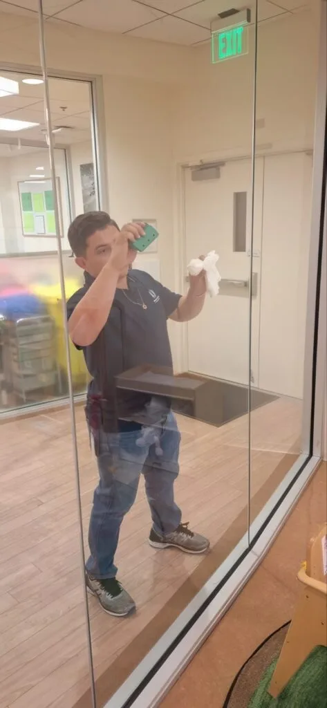 Young boy taking a selfie in a glass reflection, holding a tissue in one hand.