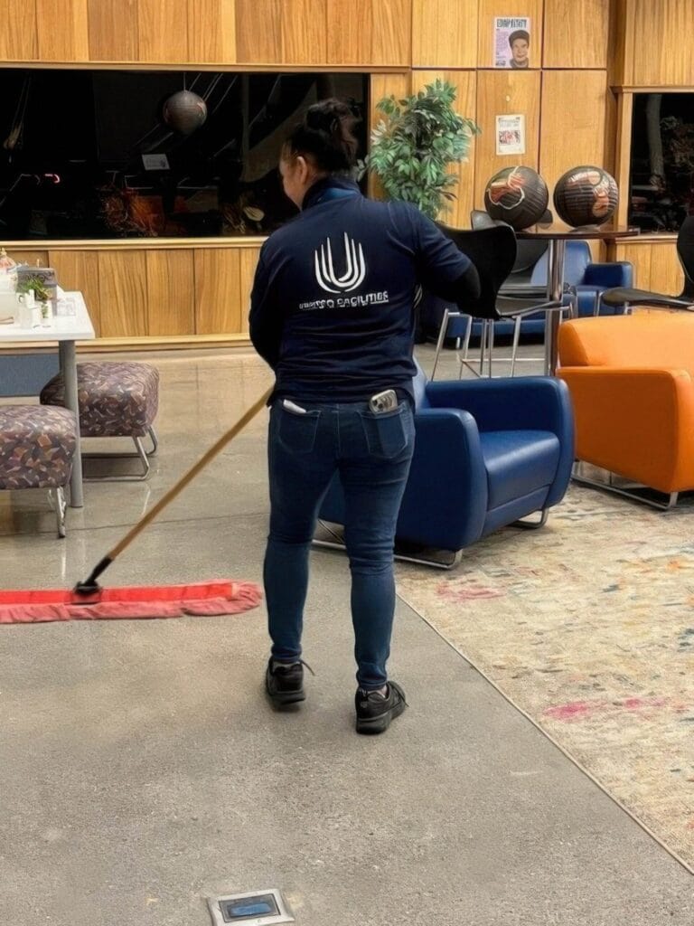 Person mopping floor in a room with blue and orange chairs, wooden wall, and decorative vases.